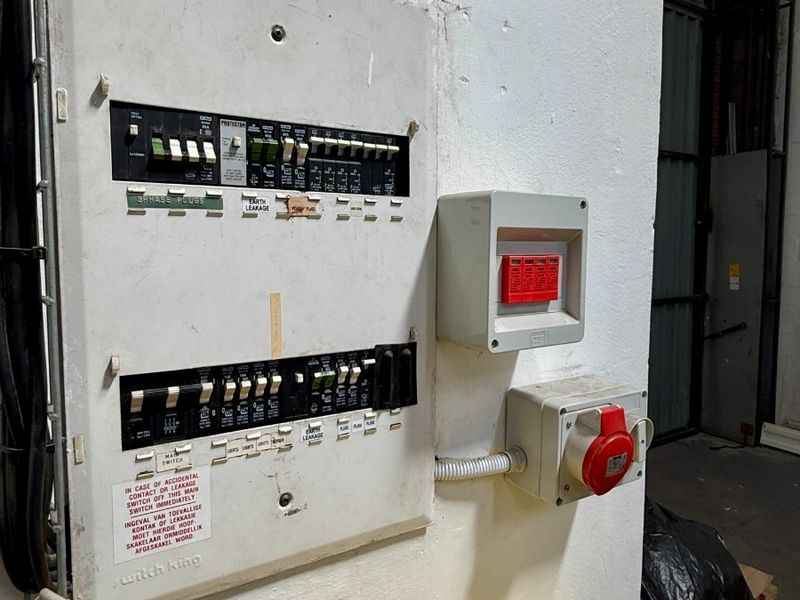Industrial utility area featuring a wall-mounted electrical distribution board with integrated circuit breakers and industrial power sockets.