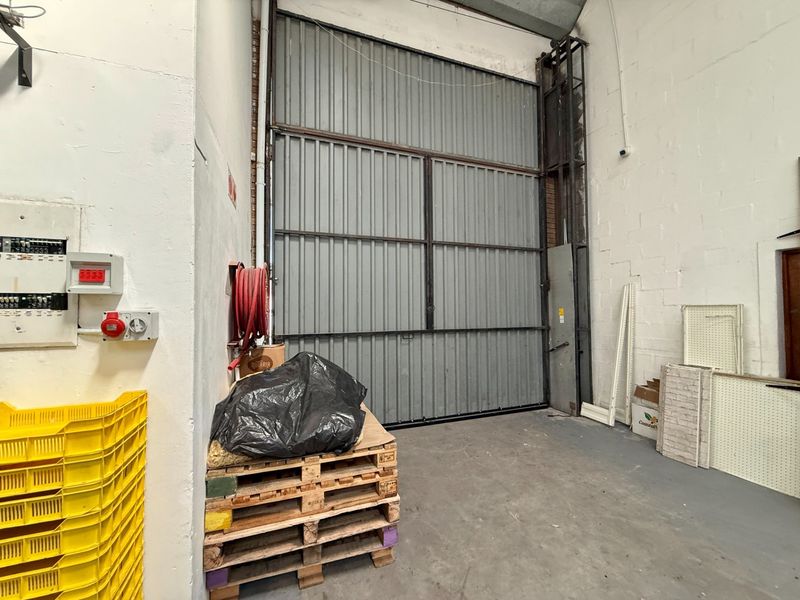 Industrial utility space featuring a large roller door, fire safety equipment, and electrical distribution board, suitable for storage or workshop operations.