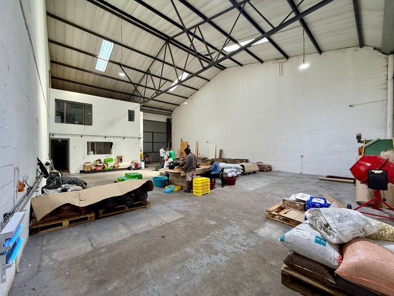 Spacious industrial warehouse unit featuring high ceilings with exposed steel trusses, concrete flooring, and a mezzanine level suitable for storage or office use.