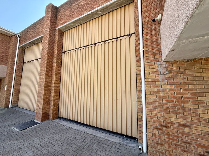 Industrial property exterior featuring large vertical roller shutter doors, face brick construction, and paved driveway access.