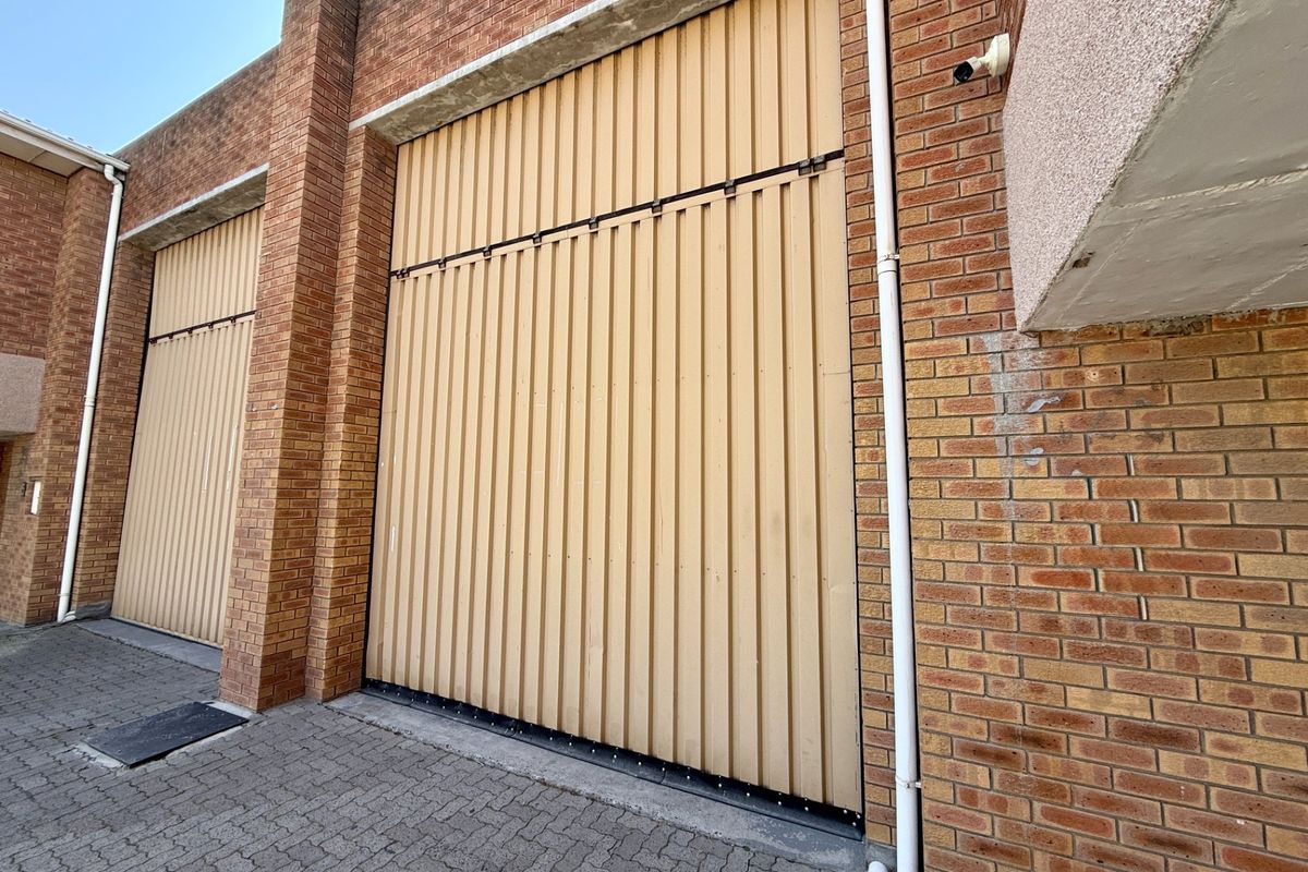 Industrial property exterior featuring large vertical roller shutter doors, face brick construction, and paved driveway access.