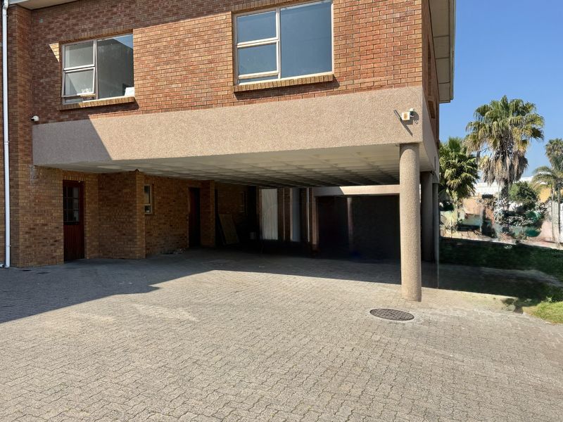 Front exterior view of an industrial property featuring a brick facade, paved driveway, and a covered parking area with a concrete support column.