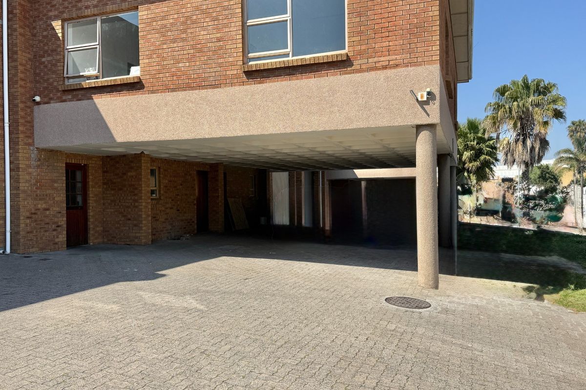 Front exterior view of an industrial property featuring a brick facade, paved driveway, and a covered parking area with a concrete support column.