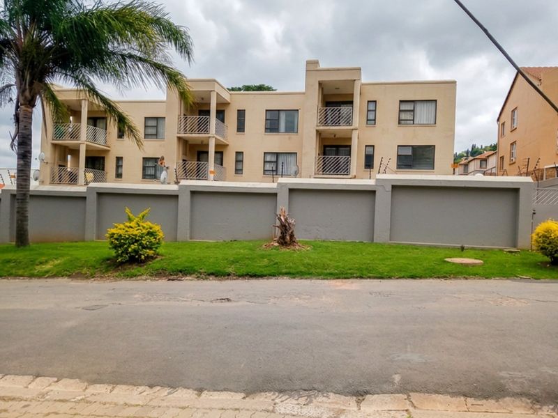 Exterior view of a multi-story apartment complex featuring balconies with metal railings and a secure perimeter wall.