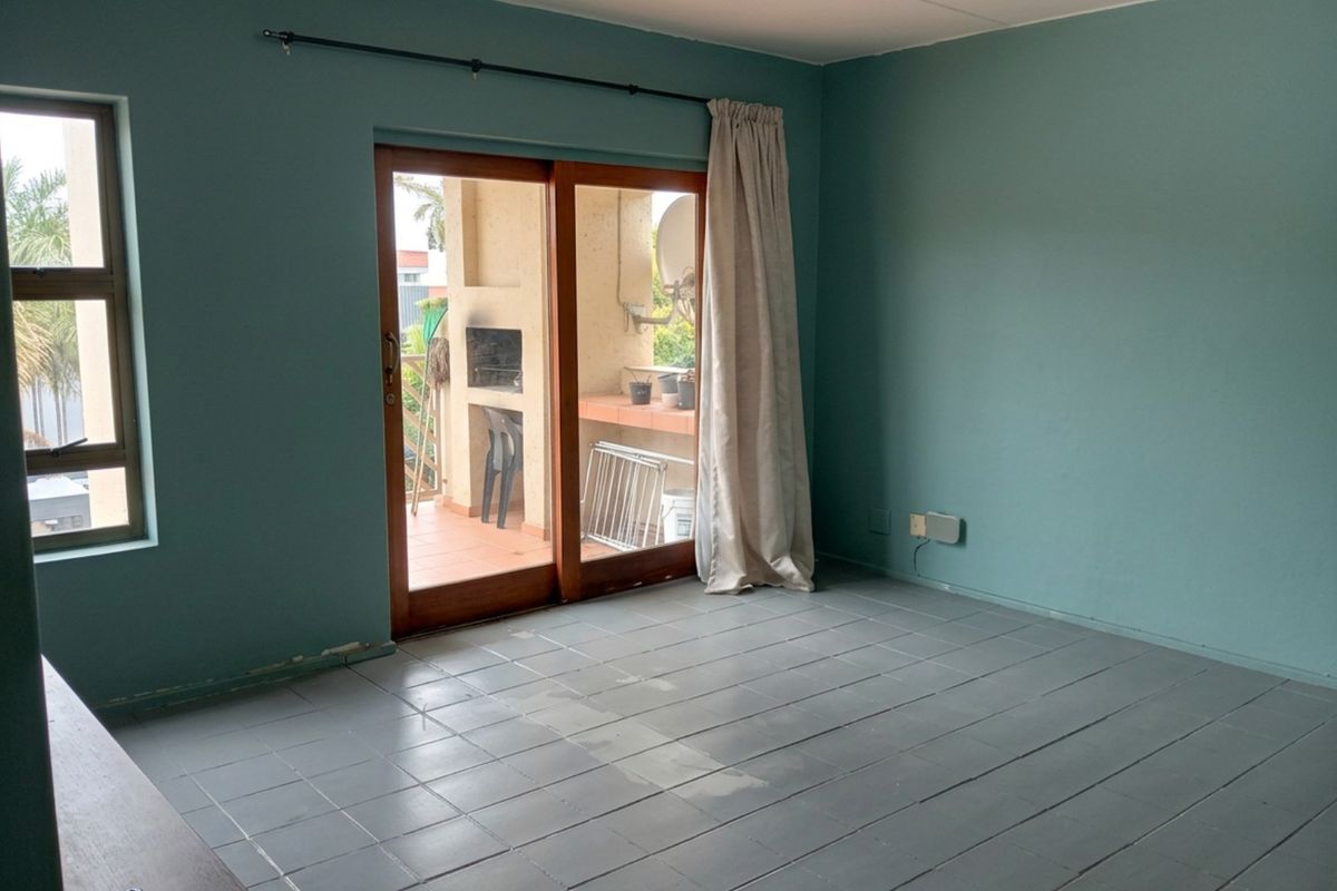An empty living room featuring tiled flooring and a sliding glass door providing access to an outdoor patio area.