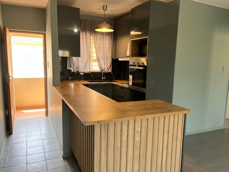 Modern kitchen featuring dark cabinetry, a wooden breakfast bar, built-in oven and microwave, and tiled flooring, with direct access to an outdoor area.