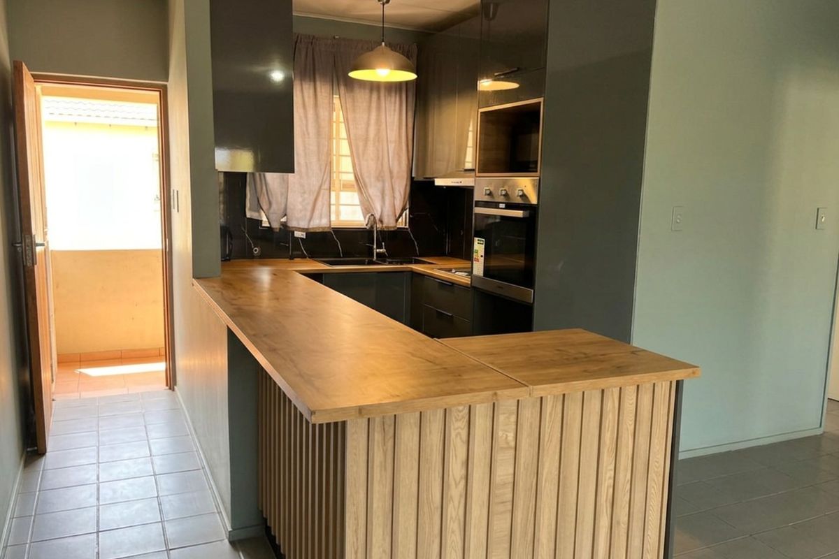 Modern kitchen featuring dark cabinetry, a wooden breakfast bar, built-in oven and microwave, and tiled flooring, with direct access to an outdoor area.