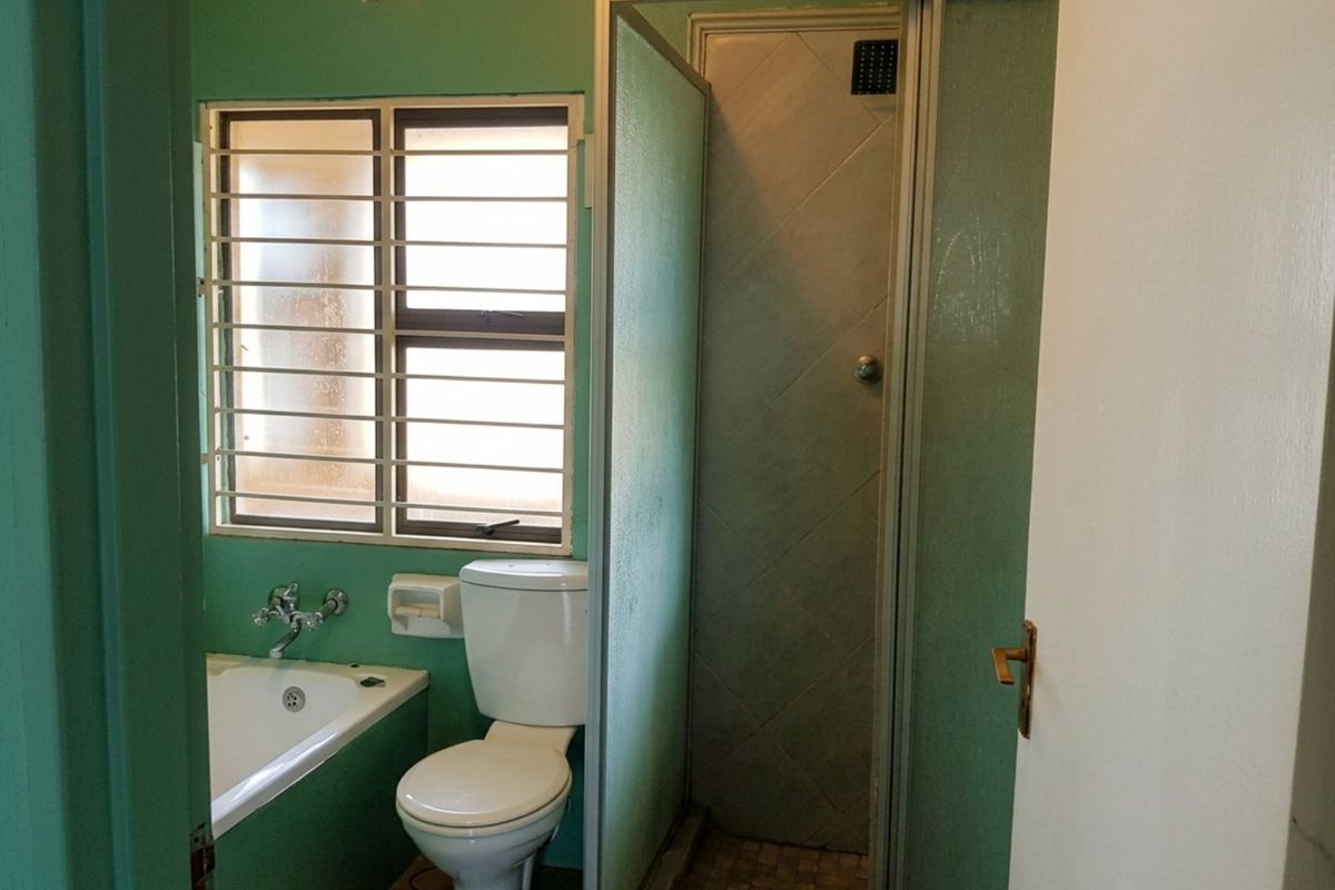 A functional bathroom featuring a built-in bathtub, toilet, and separate shower enclosure with security bars on the window.