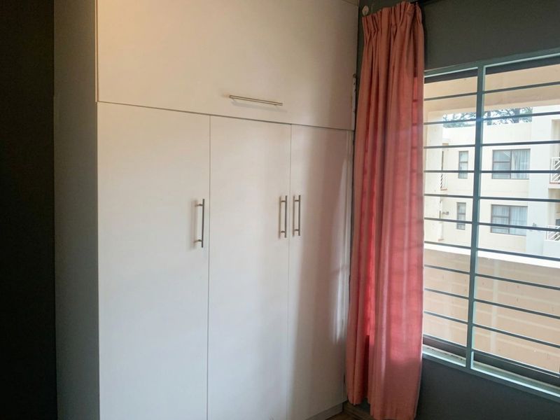 A bedroom featuring a white built-in wardrobe with overhead storage and a window fitted with security bars.