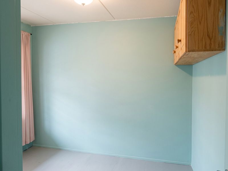 An empty bedroom featuring light blue walls, a ceiling light fixture, and wall-mounted wooden cabinetry, providing a blank canvas for potential interior updates.