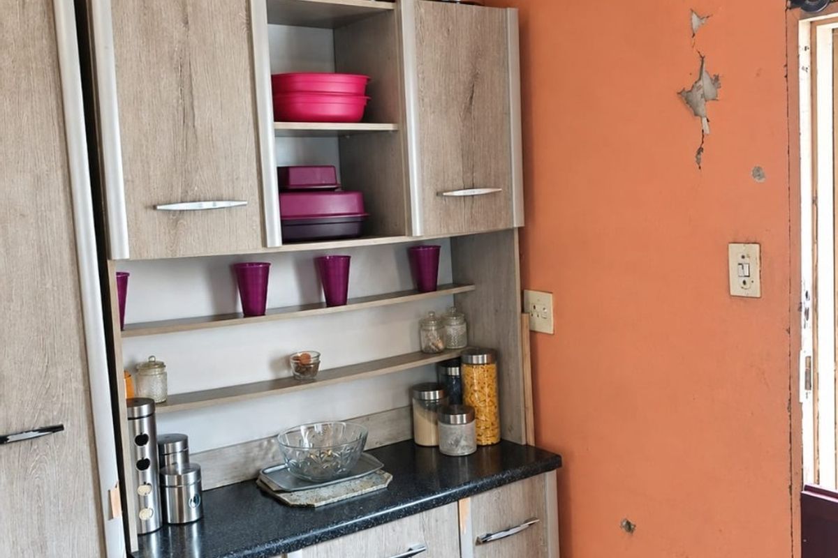 A kitchen area featuring built-in wood-look cabinetry and dark laminate countertops, currently showing significant wall surface damage and peeling paint.