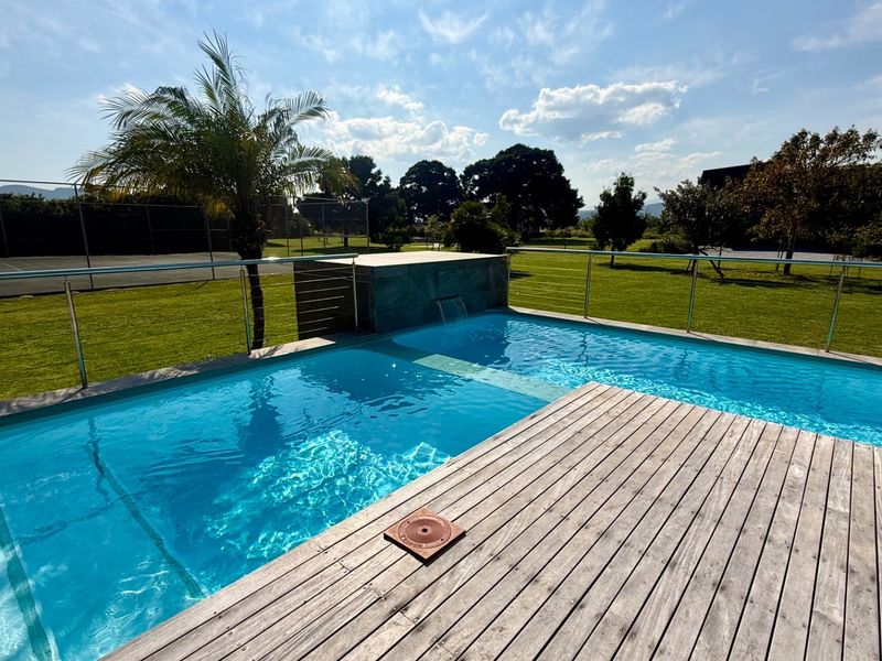 A well-maintained swimming pool area featuring timber decking, a modern water feature, and stainless steel balustrades overlooking a landscaped garden.