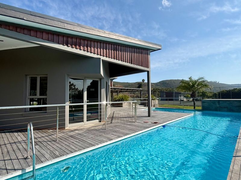 A well-maintained outdoor pool area featuring timber decking, stainless steel balustrades, and direct access to the residence via glass sliding doors.