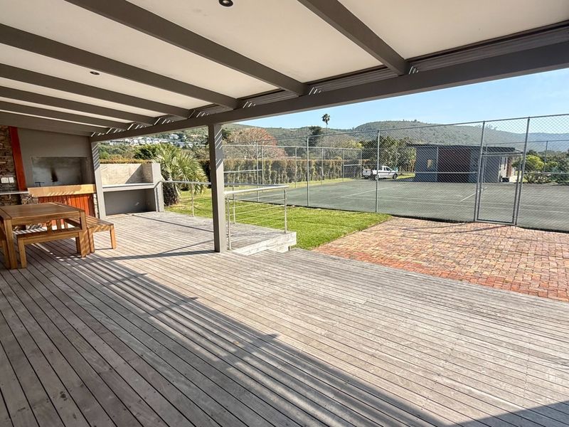 Spacious covered timber deck featuring a built-in braai area, overlooking a private tennis court and landscaped grounds.