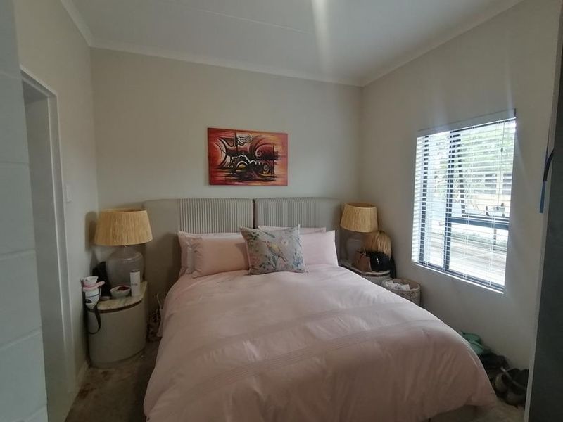 A cozy bedroom featuring neutral wall tones and a window fitted with venetian blinds, providing natural light and a comfortable living space.