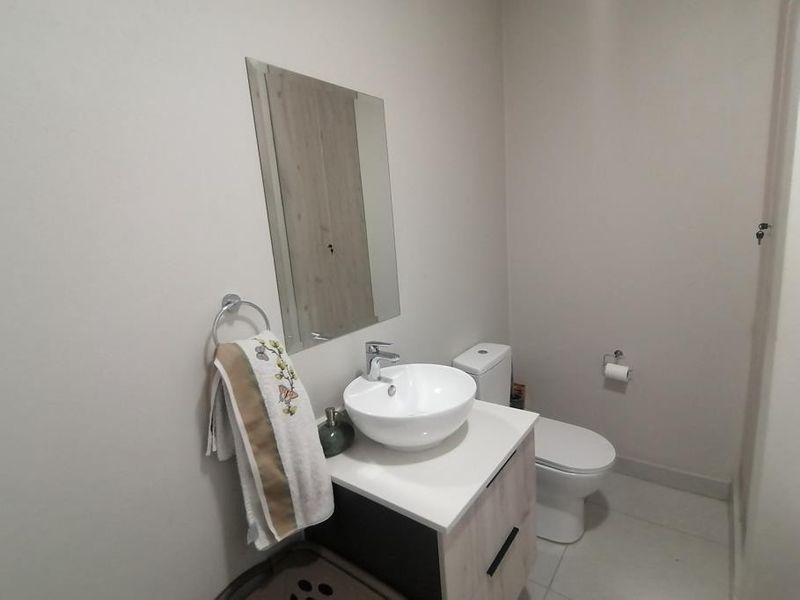 A clean and modern guest bathroom featuring a contemporary vessel sink, vanity cabinet, and wall-mounted mirror.