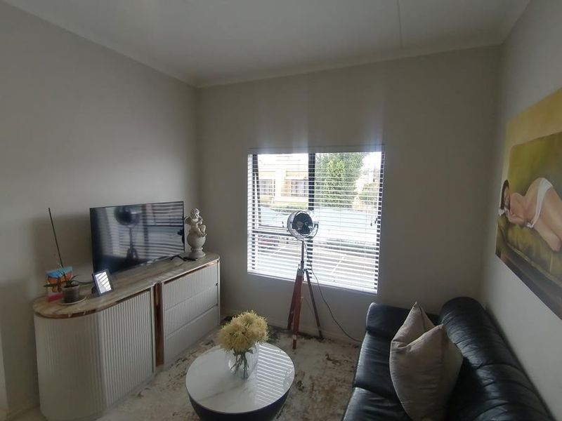 A compact living room featuring neutral wall tones, a large window with venetian blinds, and coving detail.