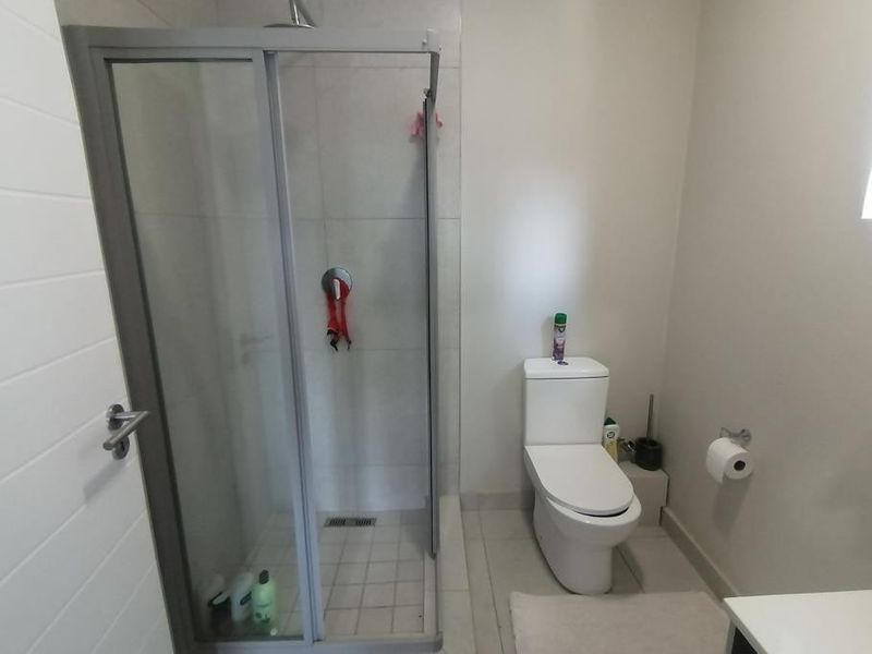 A functional bathroom featuring a glass-enclosed shower, a modern toilet, and neutral wall and floor tiling.