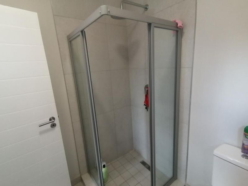A clean and functional bathroom featuring a corner shower enclosure with tiled walls and flooring, alongside a standard toilet.