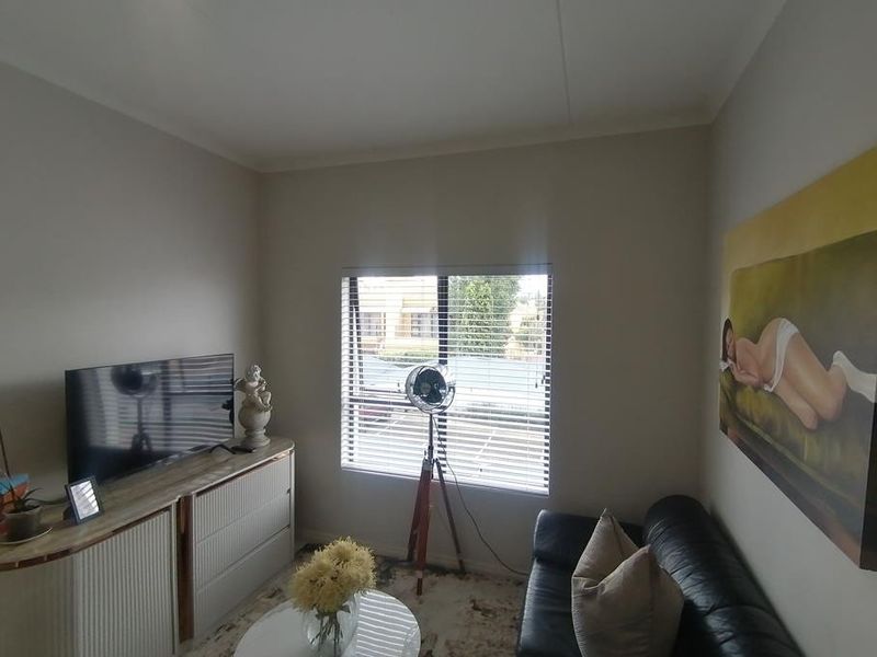 A comfortable living room featuring neutral walls and venetian blinds, providing a bright and functional space for relaxation.