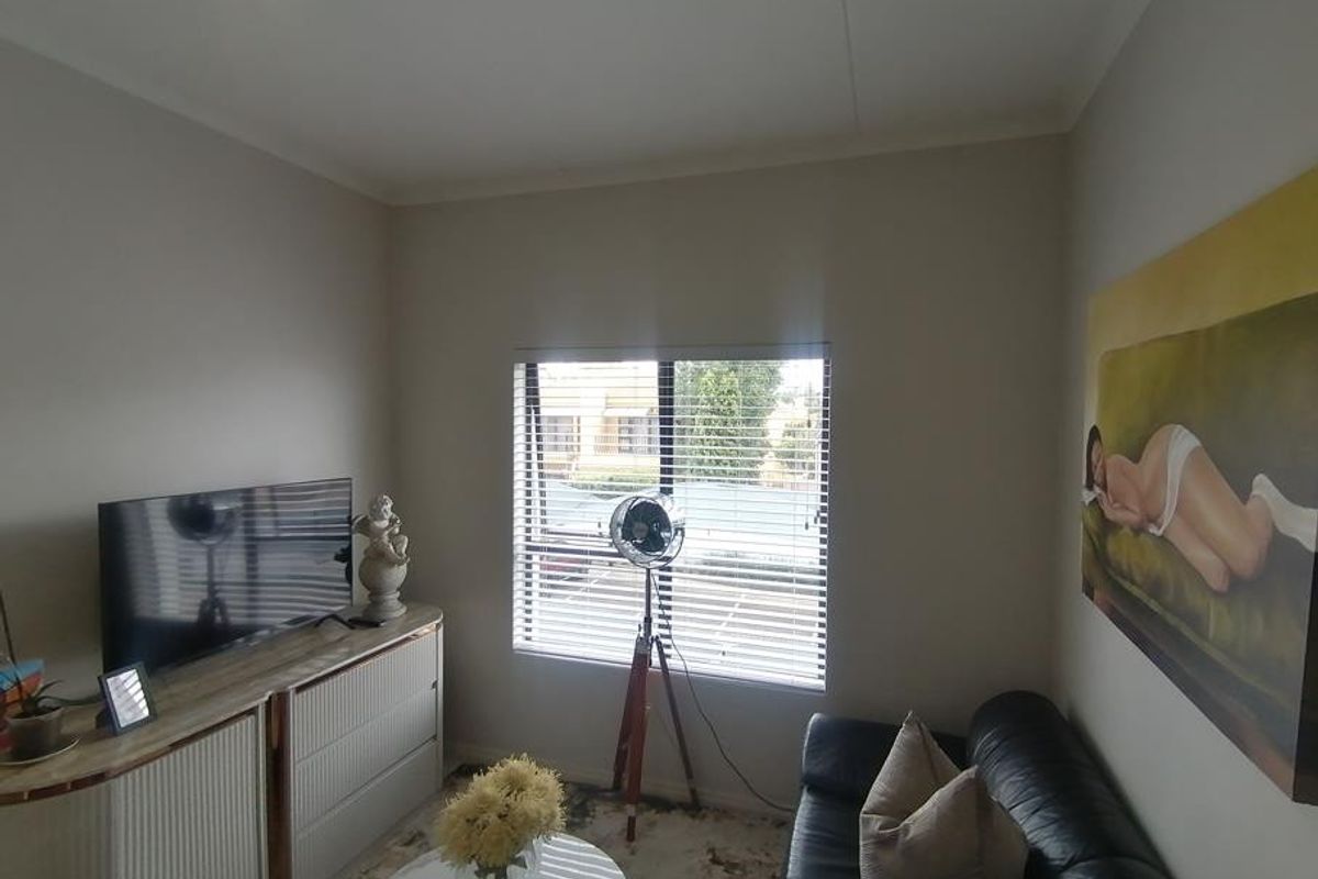 A comfortable living room featuring neutral walls and venetian blinds, providing a bright and functional space for relaxation.