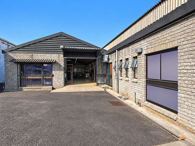 Industrial property exterior featuring concrete block masonry, metal roofing, and a paved driveway with secure access points and functional window configurations.