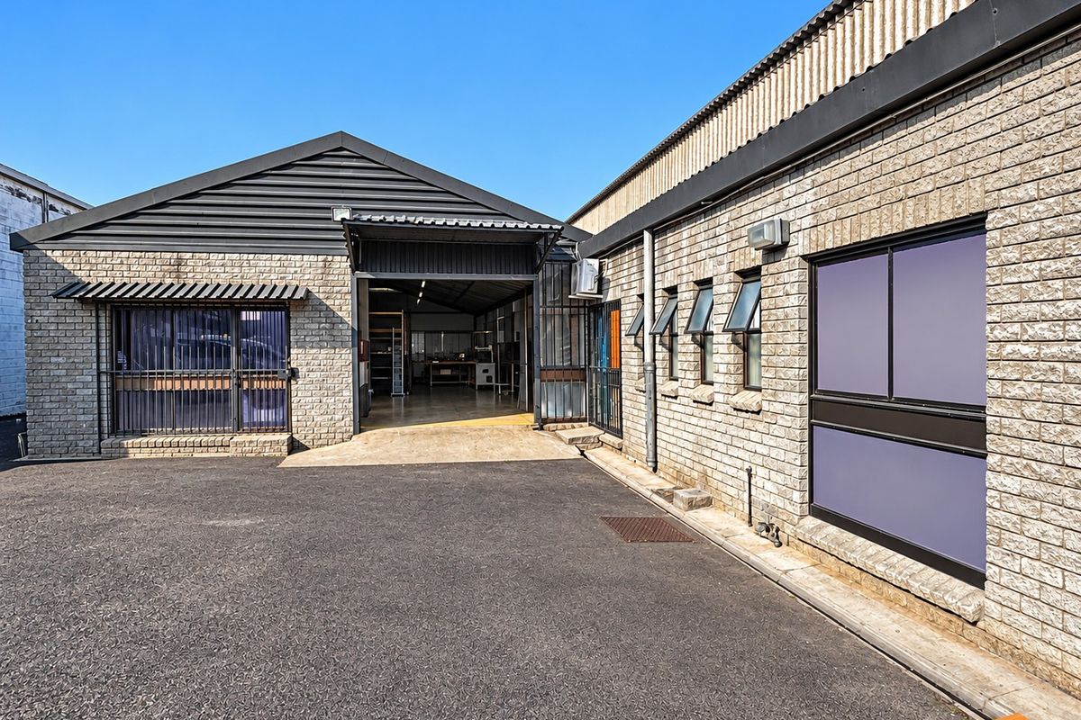 Industrial property exterior featuring concrete block masonry, metal roofing, and a paved driveway with secure access points and functional window configurations.