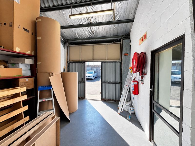 Industrial garage space featuring a painted concrete floor, exposed steel roof structure, and essential fire safety equipment including a hose reel and extinguisher.