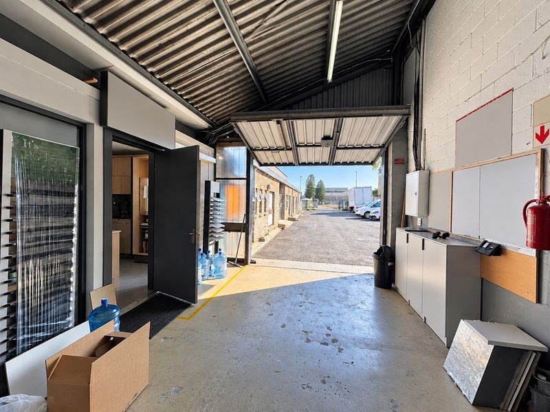 Industrial utility space featuring concrete flooring, corrugated metal roofing, and direct access to an external yard area through a large roller door.
