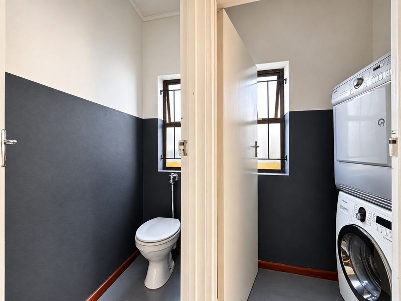 A functional laundry area featuring a separate toilet compartment, finished with modern two-tone wall paint and secure window bars.