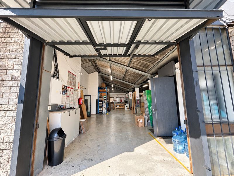 Spacious industrial garage or workshop area featuring high ceilings with exposed steel trusses, concrete flooring, and a large industrial roller door entrance.