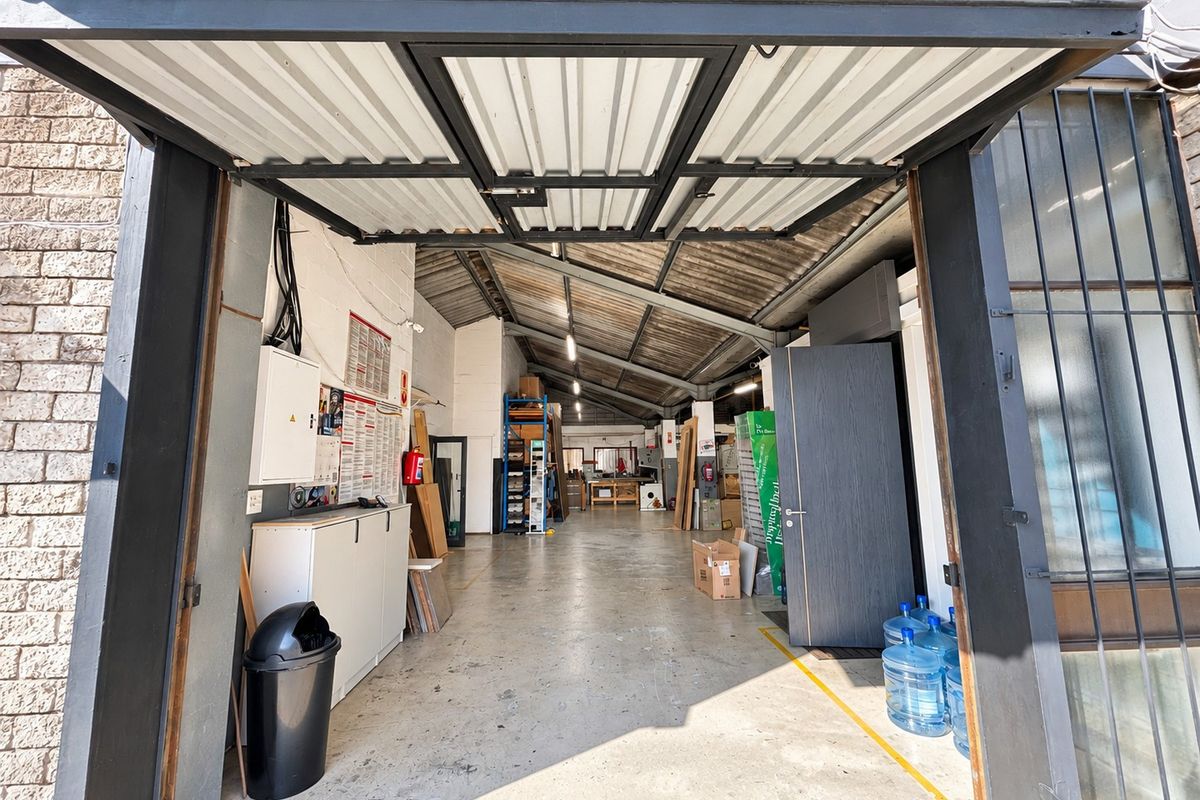 Spacious industrial garage or workshop area featuring high ceilings with exposed steel trusses, concrete flooring, and a large industrial roller door entrance.