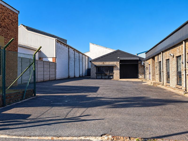 Rear industrial yard area featuring asphalt paving, security fencing, and brick building facades with secure access points.