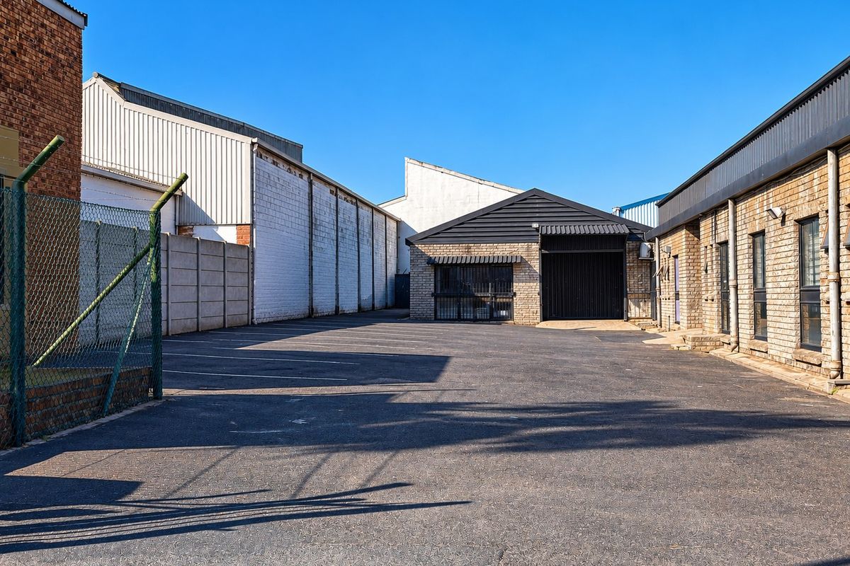 Rear industrial yard area featuring asphalt paving, security fencing, and brick building facades with secure access points.