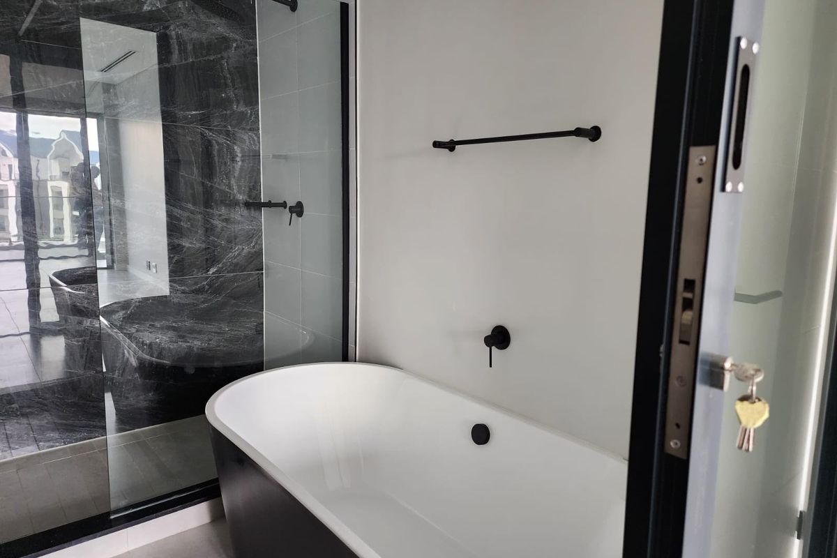 Modern bathroom featuring a sleek freestanding bathtub, a spacious walk-in shower with marble-look tiling, and contemporary black matte fixtures.