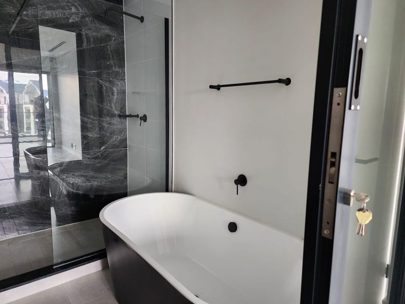 Modern bathroom featuring a sleek freestanding bathtub, a spacious walk-in shower with marble-look tiling, and contemporary black matte fixtures.