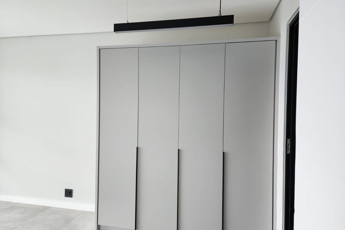 A clean, modern bedroom featuring neutral grey built-in wardrobes, contemporary pendant lighting, and sleek tiled flooring.