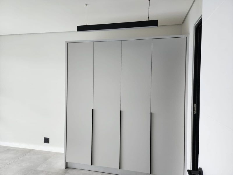 A clean, modern bedroom featuring neutral grey built-in wardrobes, contemporary pendant lighting, and sleek tiled flooring.