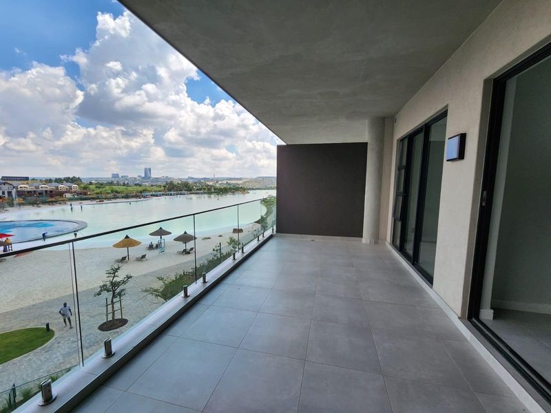 Spacious covered balcony featuring modern tiled flooring, a sleek glass balustrade, and expansive views overlooking the lagoon and beach area.