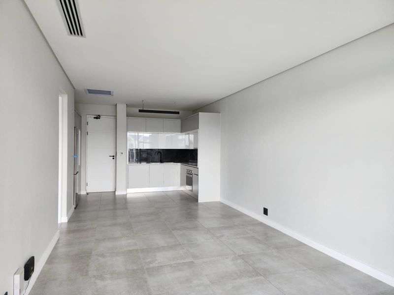 Modern open-plan living area featuring a sleek kitchen with built-in cabinetry, integrated oven, and contemporary tiled flooring throughout.