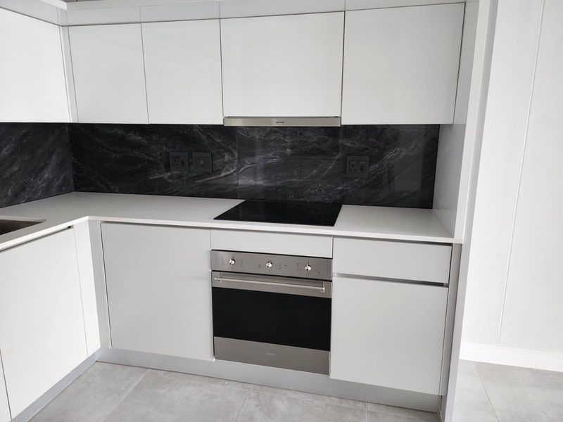 Modern kitchen featuring white gloss cabinetry, stone countertops, a striking black marble-effect splashback, and integrated stainless steel appliances.