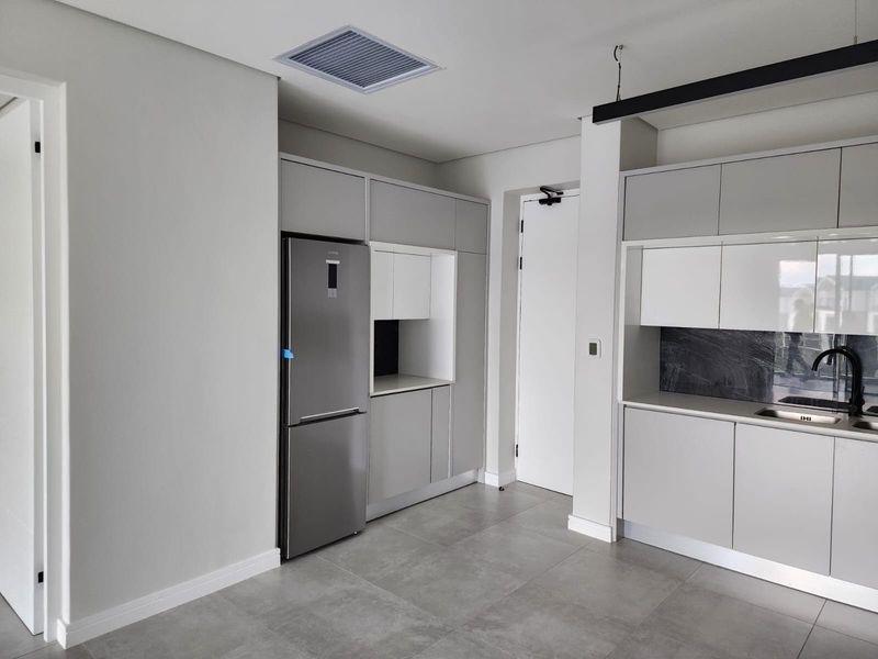 Modern kitchen featuring sleek grey cabinetry, stone countertops, integrated sink, and high-quality tiled flooring in a clean, contemporary apartment setting.