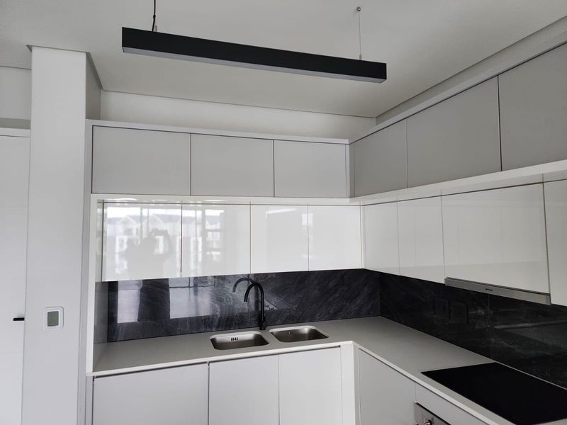Modern kitchen featuring sleek white cabinetry, dark stone-look splashback, integrated appliances, and a contemporary double sink with a black mixer tap.