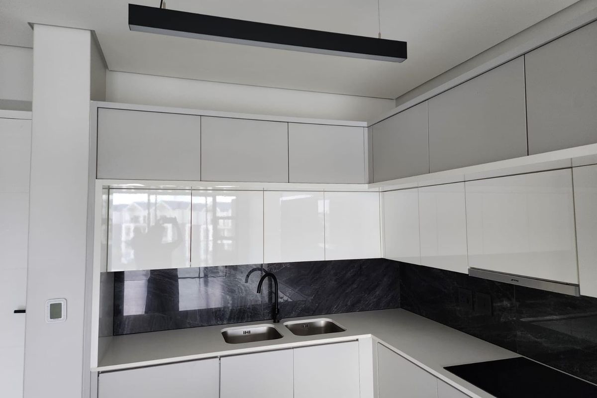 Modern kitchen featuring sleek white cabinetry, dark stone-look splashback, integrated appliances, and a contemporary double sink with a black mixer tap.