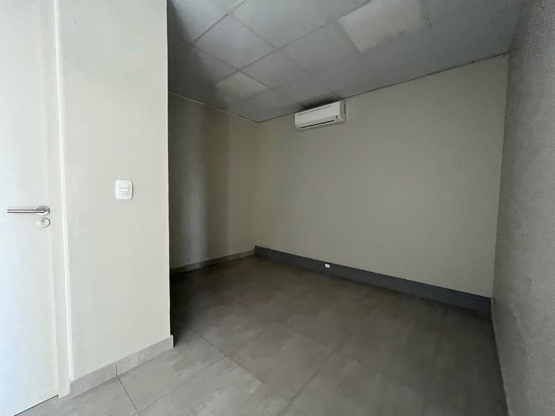 A clean, empty office space featuring tiled flooring, a drop ceiling, and a wall-mounted split-system air conditioning unit.