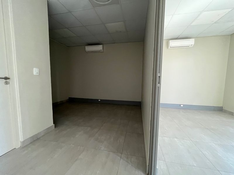 A clean, empty office space featuring tiled flooring, suspended ceilings, and wall-mounted air conditioning units, suitable for professional use.