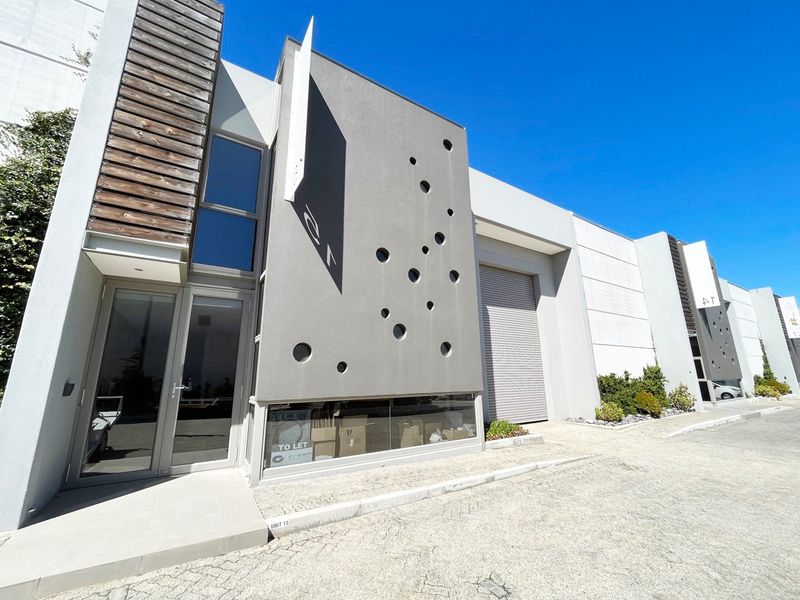 Modern industrial unit exterior featuring a contemporary facade with decorative circular cutouts, a roller shutter door, and a glass-fronted entrance.
