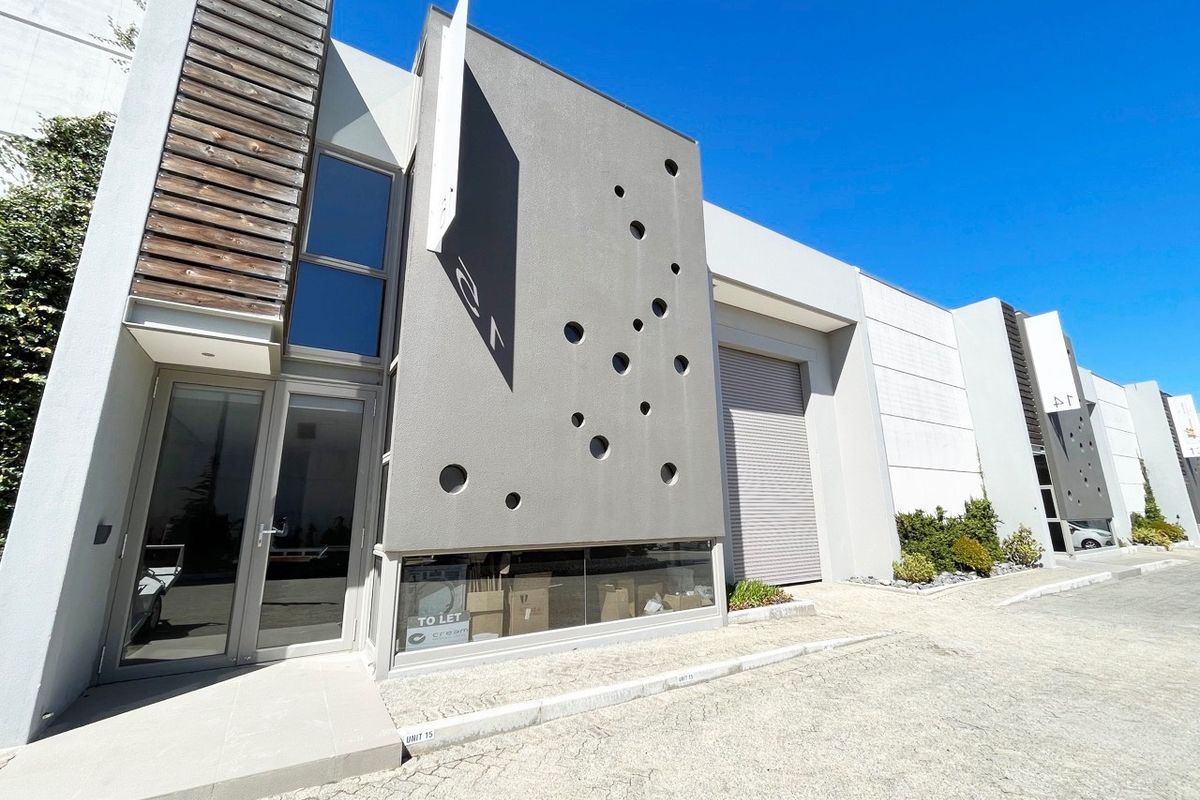 Modern industrial unit exterior featuring a contemporary facade with decorative circular cutouts, a roller shutter door, and a glass-fronted entrance.