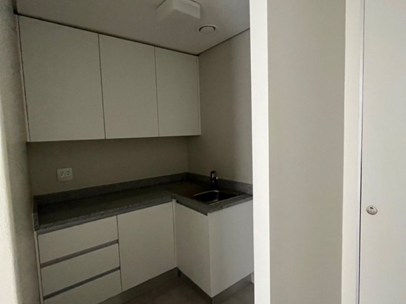 A compact, clean scullery or kitchenette area featuring modern white cabinetry, stone countertops, and a stainless steel sink.