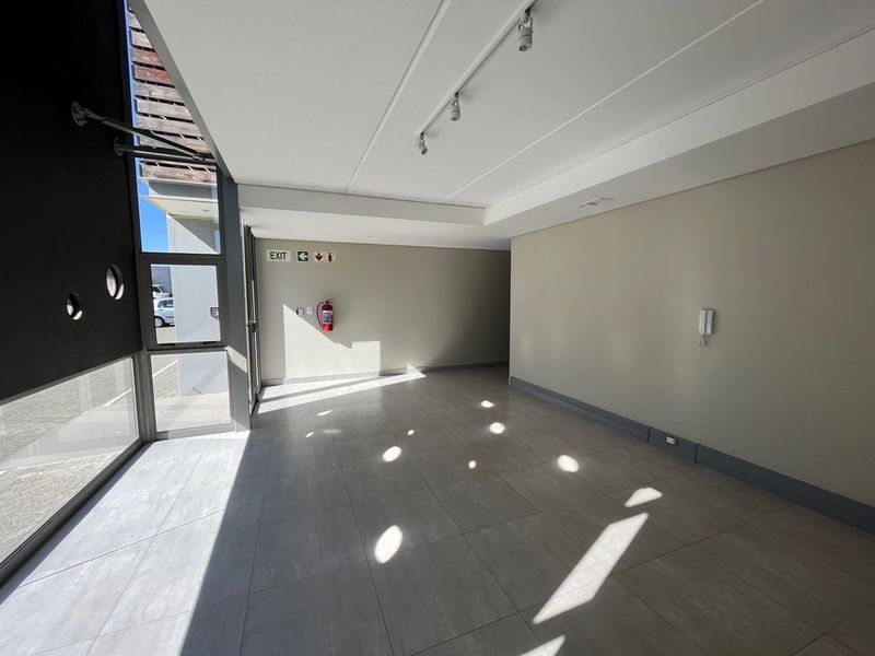 A bright, modern industrial entrance area featuring large glass windows, tiled flooring, track lighting, and essential safety fixtures.